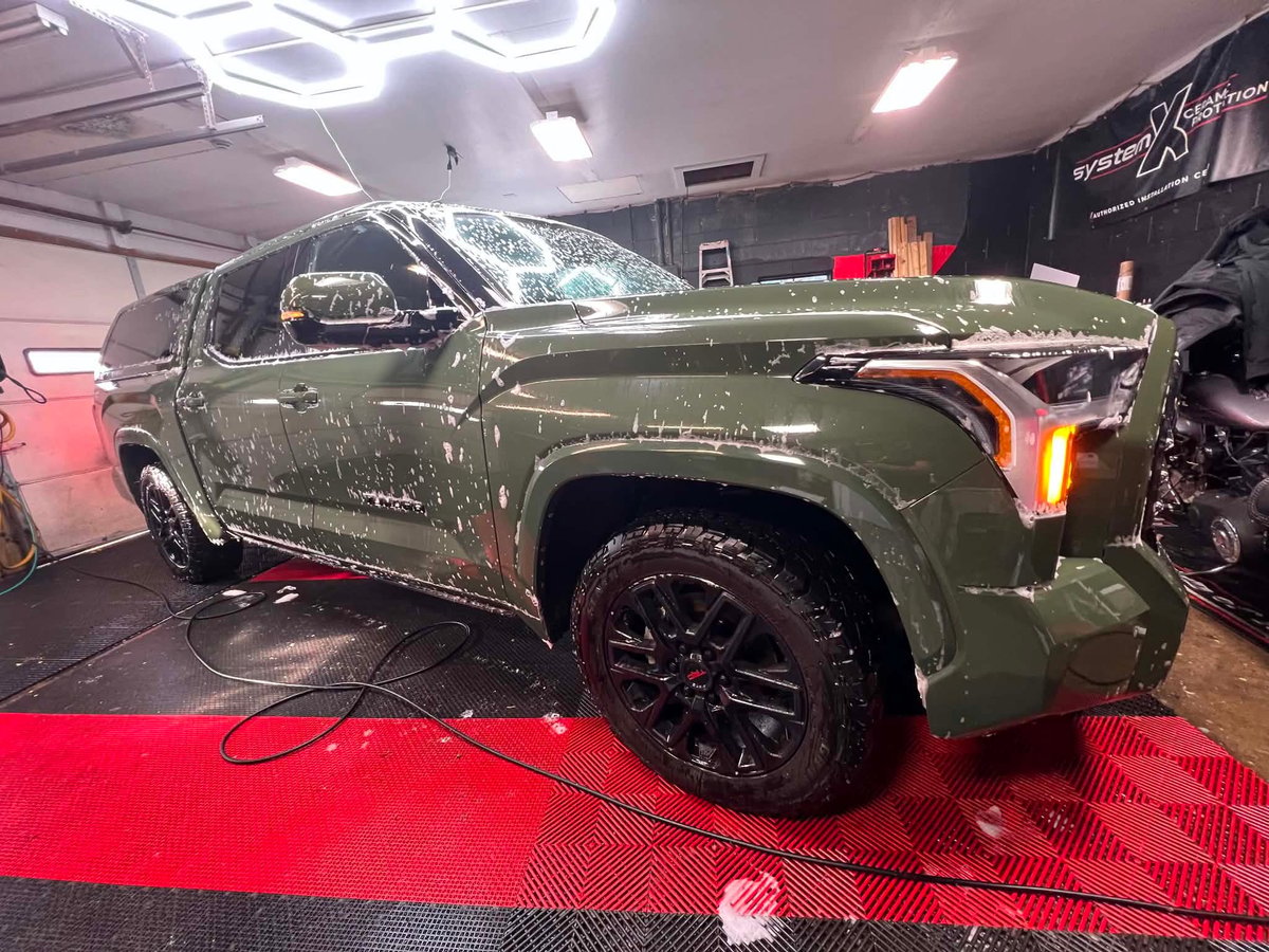 Olive green pickup truck getting a foam pre-soak wash in the shop